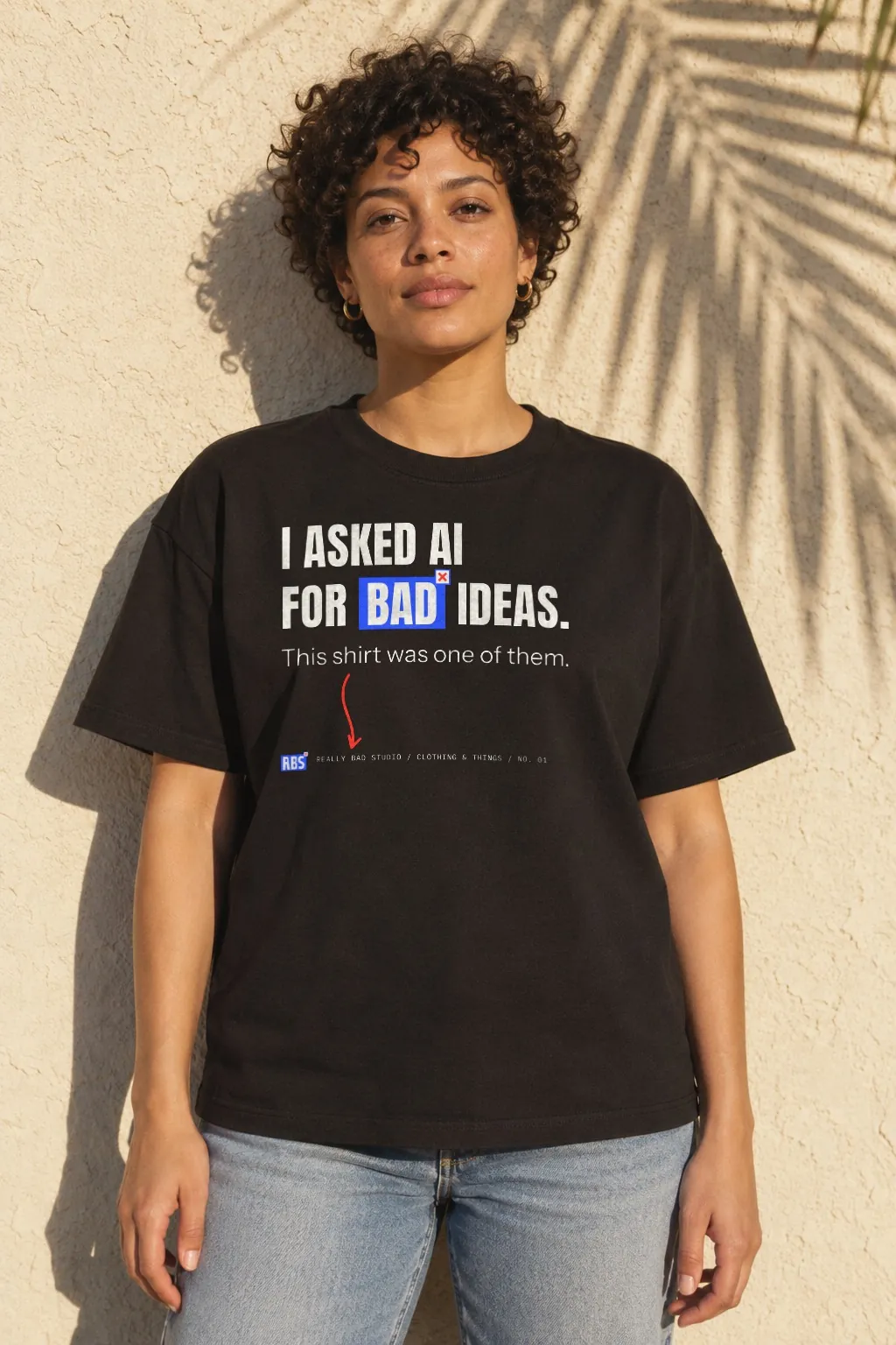 A woman with short curly hair in a black tee printed: I asked AI for bad ideas. This shirt was one of them.