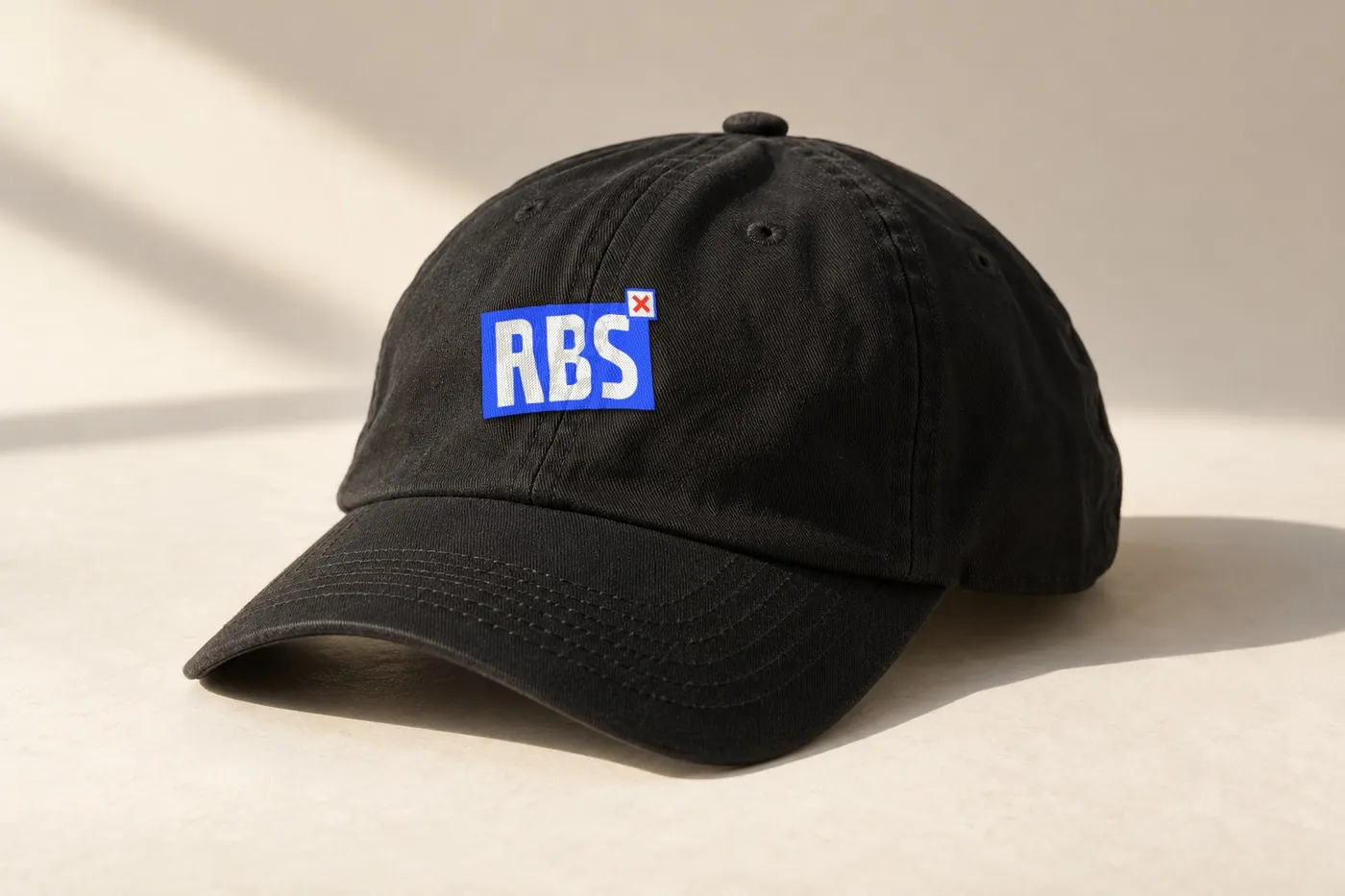 A black six-panel cap with the RBS tab embroidered on the front.